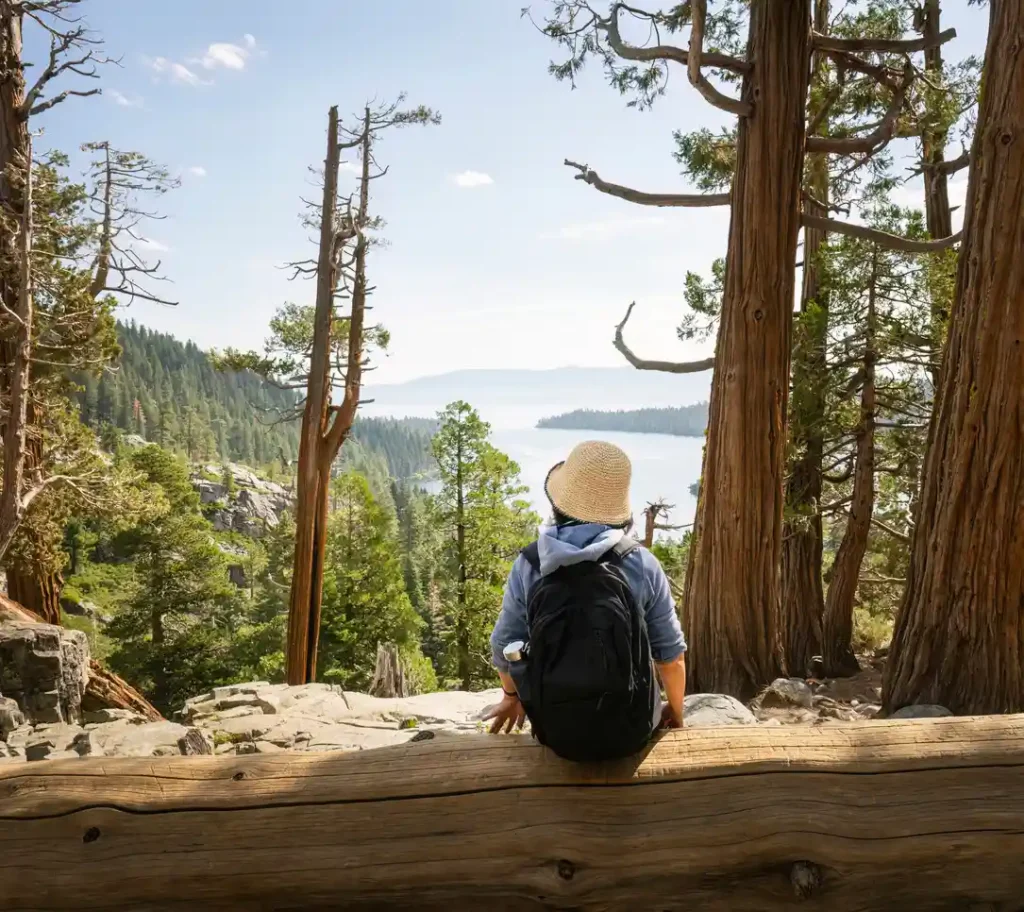 Girl in a bucket hat sitting on a log looking out at the stunning Emerald Bay in Lake Tahoe